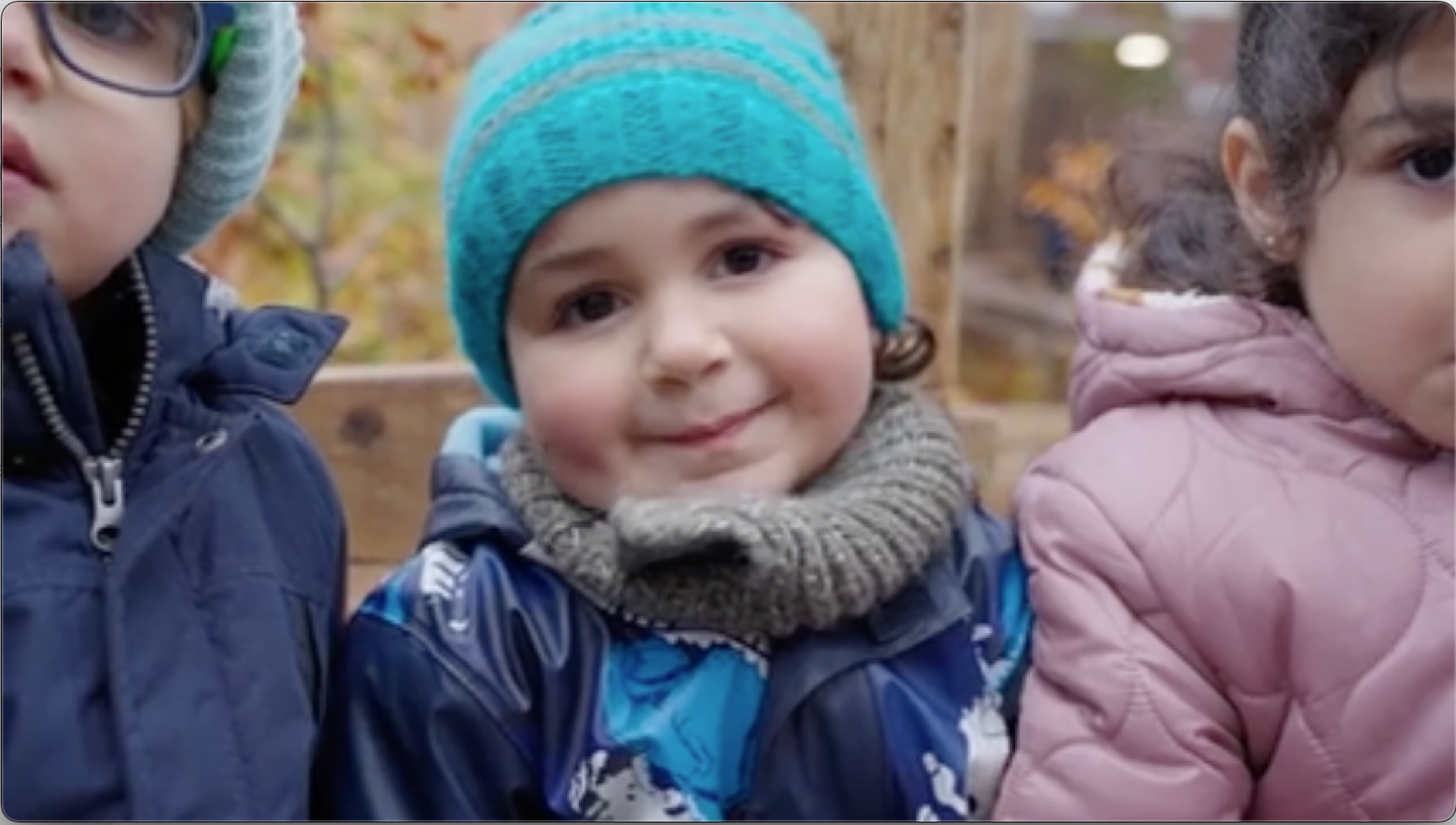 A young person and person wearing knit caps, bonnets, and jackets are playing outdoors in the winter.